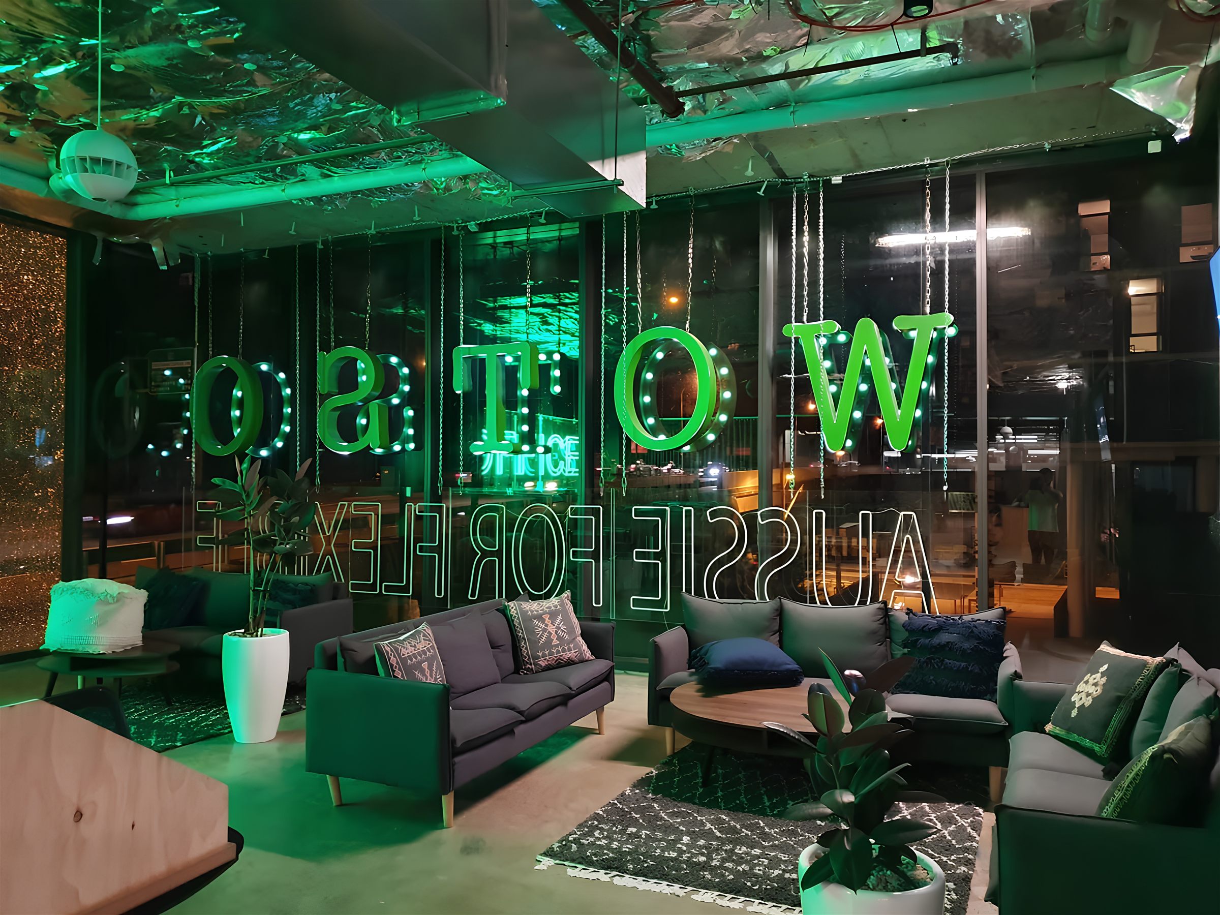 Reversed WOTSO neon channel letters glowing green in a full-height window at night